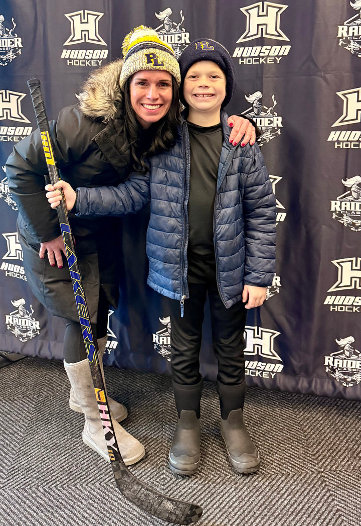 Woman and child posing with a custom hockey stick from HKY IQ in front of a Hudson Hockey backdrop
